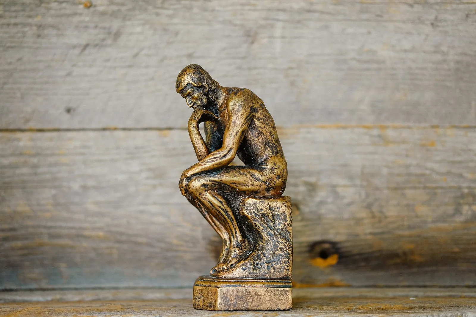 A small bronze replica of Rodin’s The Thinker on a weathered wooden surface.
