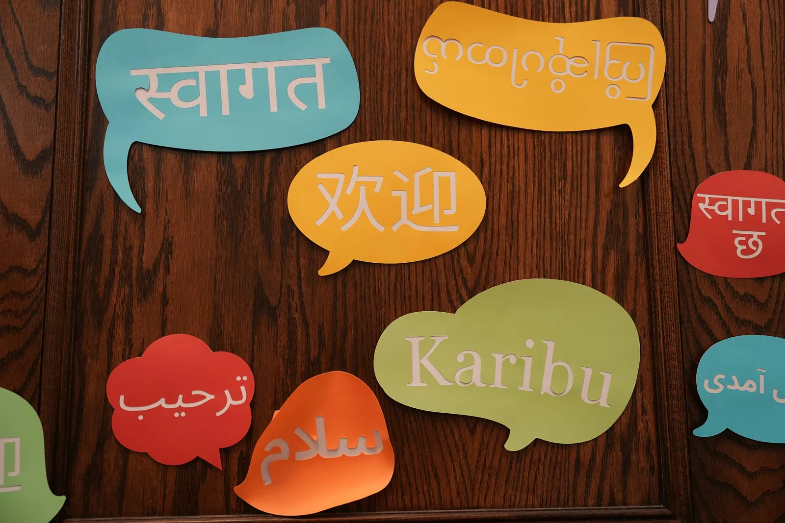 Speech bubbles on a wooden wall saying “welcome” in many languages and scripts.